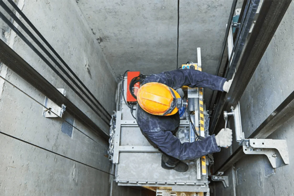 Técnico en mantenimiento industrial dentro del hueco de un ascensor con casco y guantes