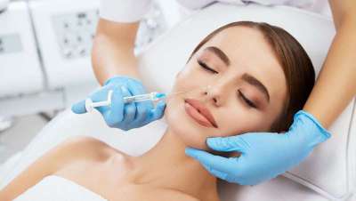 Mujer recibiendo infiltración facial estética con jeringa, profesional con guantes — cursos online