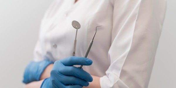 Profesional dental con espejo y explorador en guantes azules, formación para el empleo