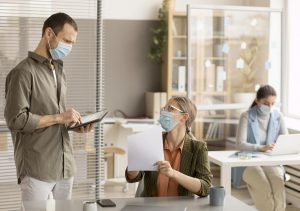 Hombre con tablet y compañera con documento en oficina con mascarillas — formación para el empleo