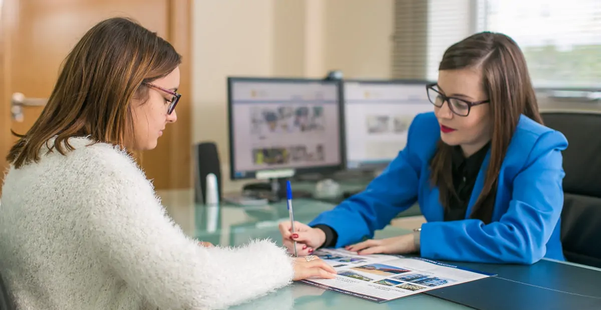 Asesora señalando un folleto mientras una mujer firma, formación para el empleo