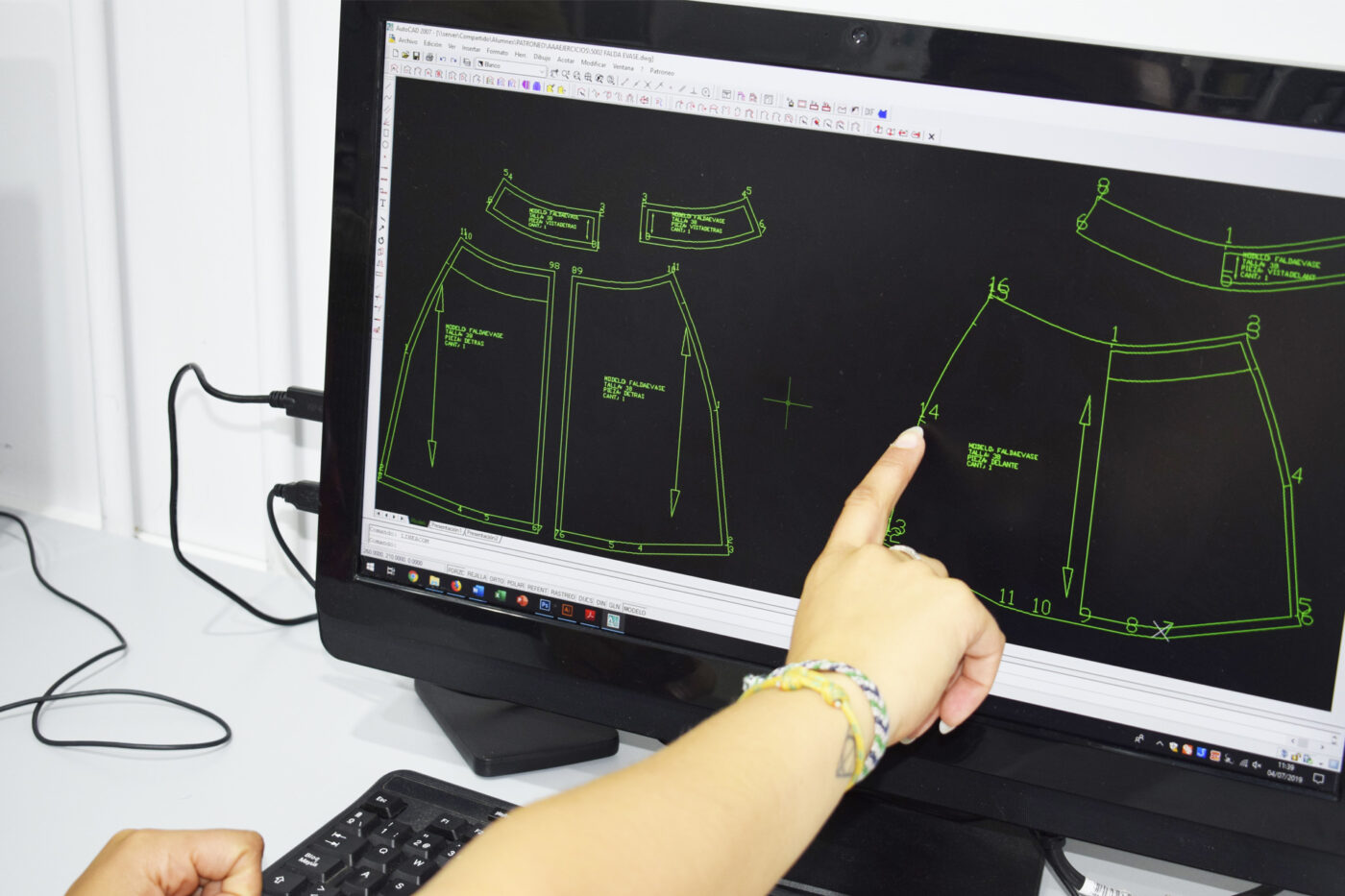 Patrones de prendas en pantalla de ordenador señalados por una mano — cursos online