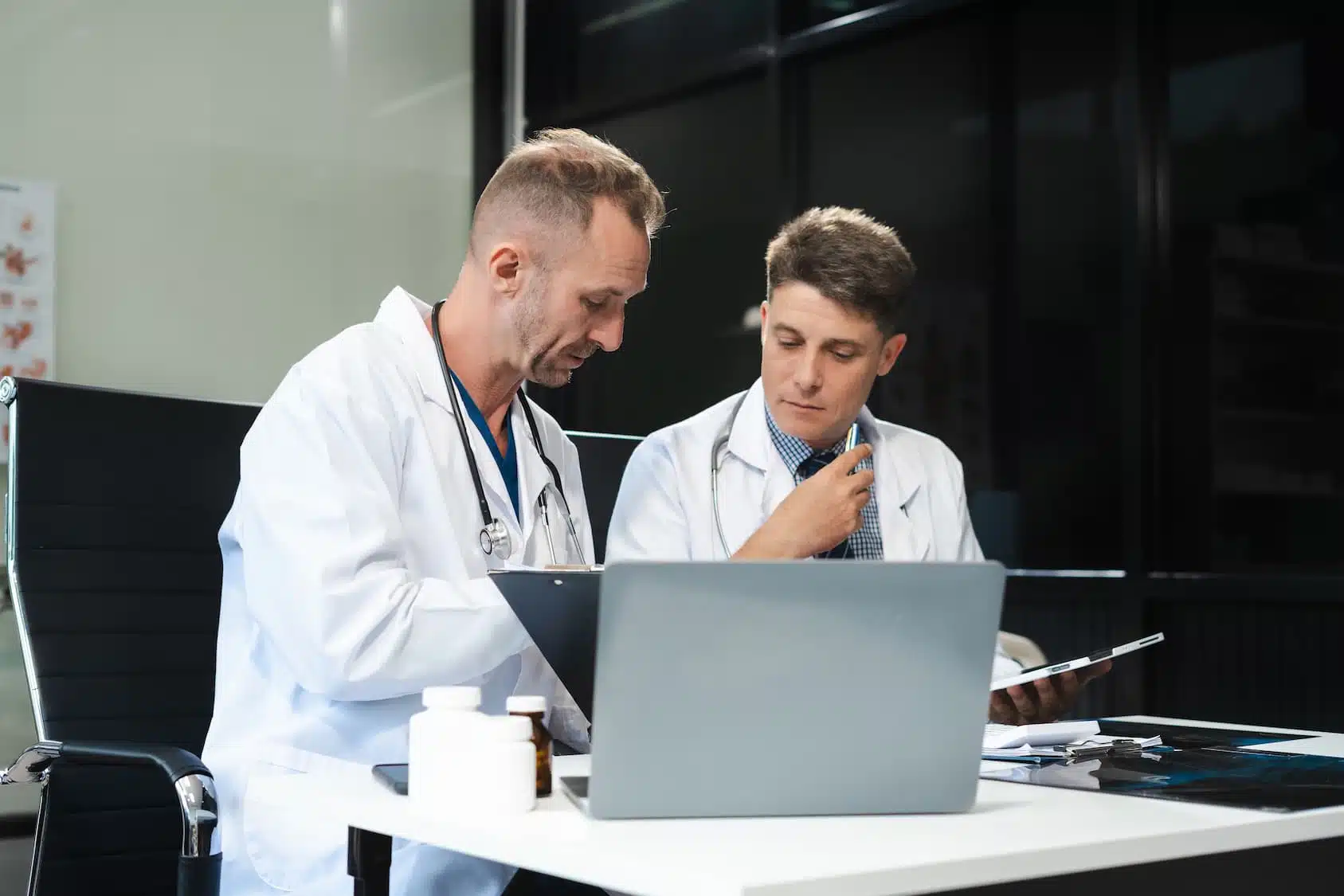 Dos médicos con batas y estetoscopios revisando un portátil y documentación — cursos online