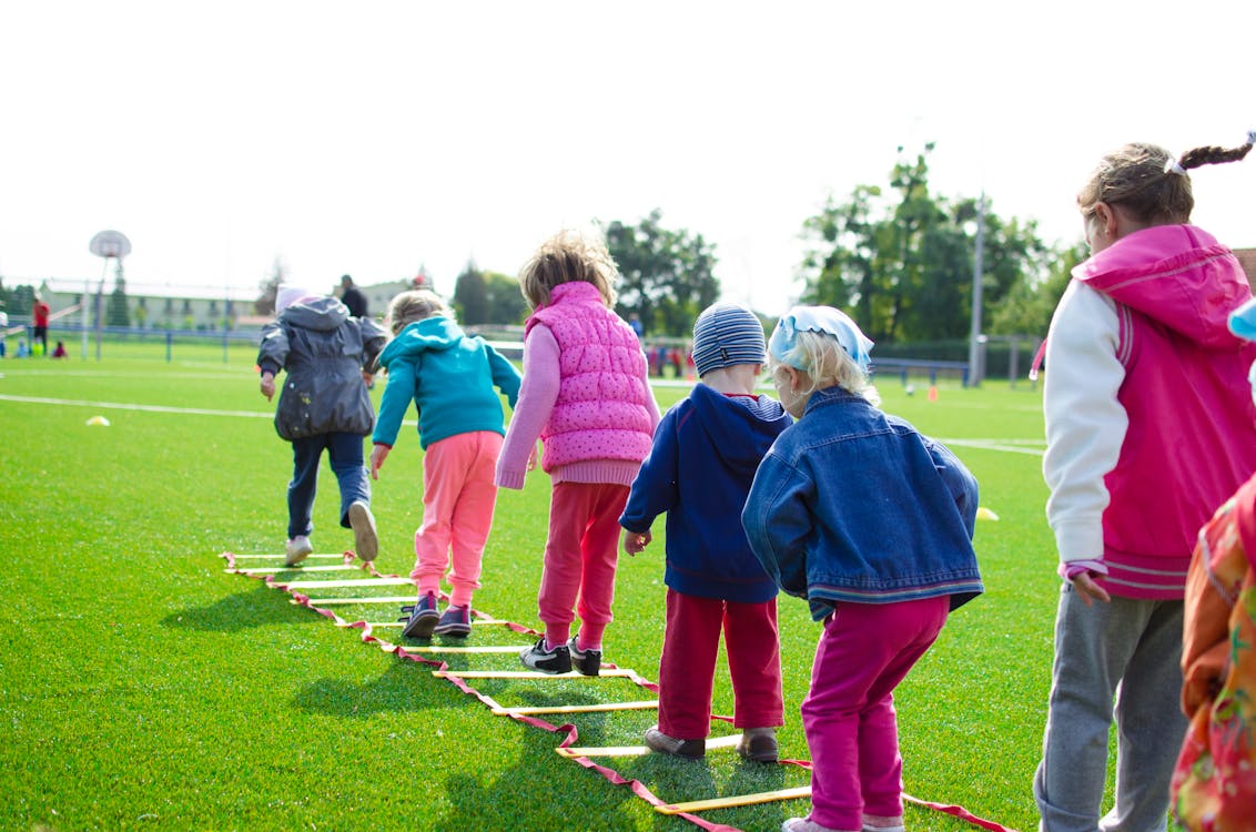 Niños en escalera de agilidad sobre césped, formación para asociaciones