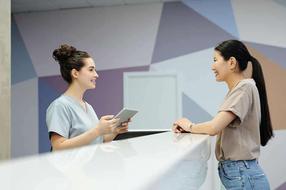 Recepcionista sanitaria con tablet atendiendo a paciente en mostrador — formación para el empleo