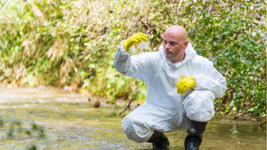 Técnico con traje protector y guantes tomando muestra de agua en un arroyo — formación para el empleo