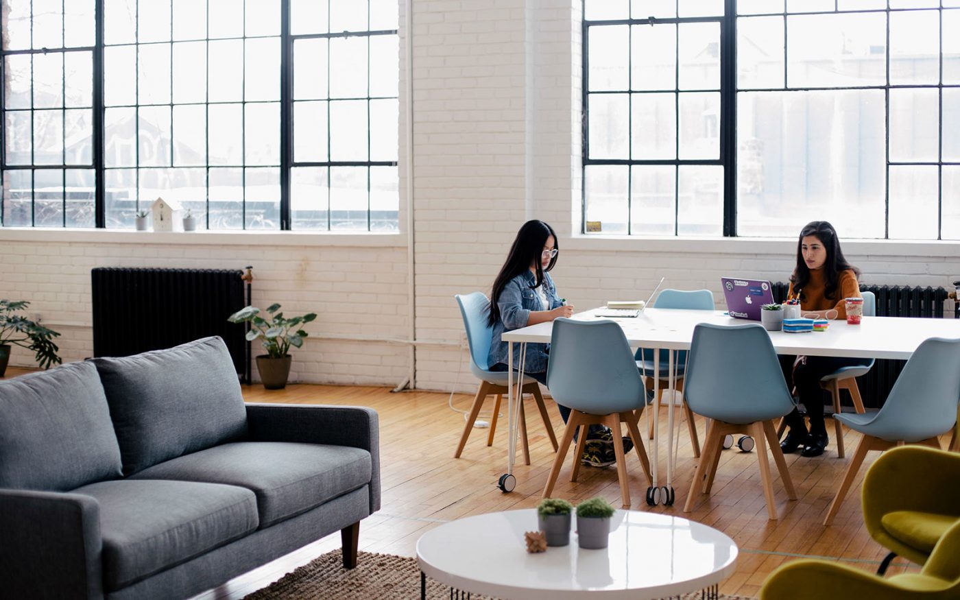 Espacio de trabajo luminoso con dos mujeres en una mesa, una usando un portátil; cursos online
