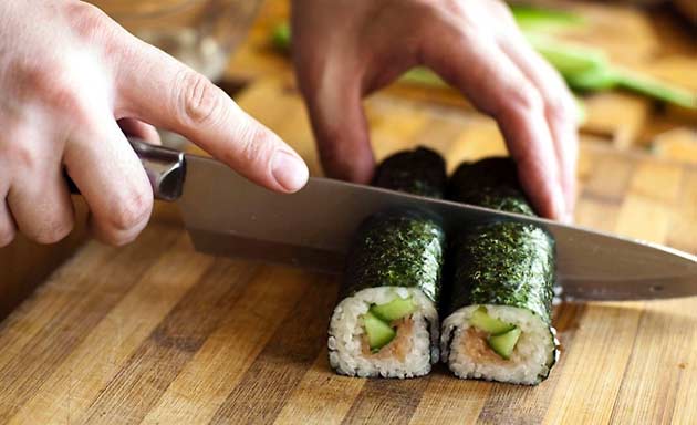 Maki de sushi cortado con cuchillo sobre tabla de madera — cursos online