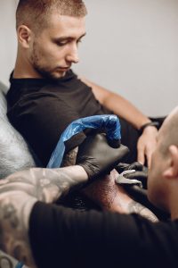 Tatuador tatuando el antebrazo de un cliente, certificado de profesionalidad