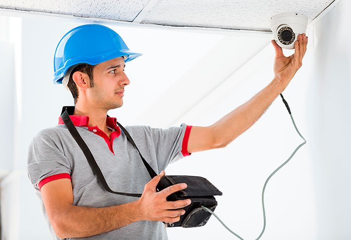 Técnico con casco azul instalando cámara de seguridad, formación para el empleo