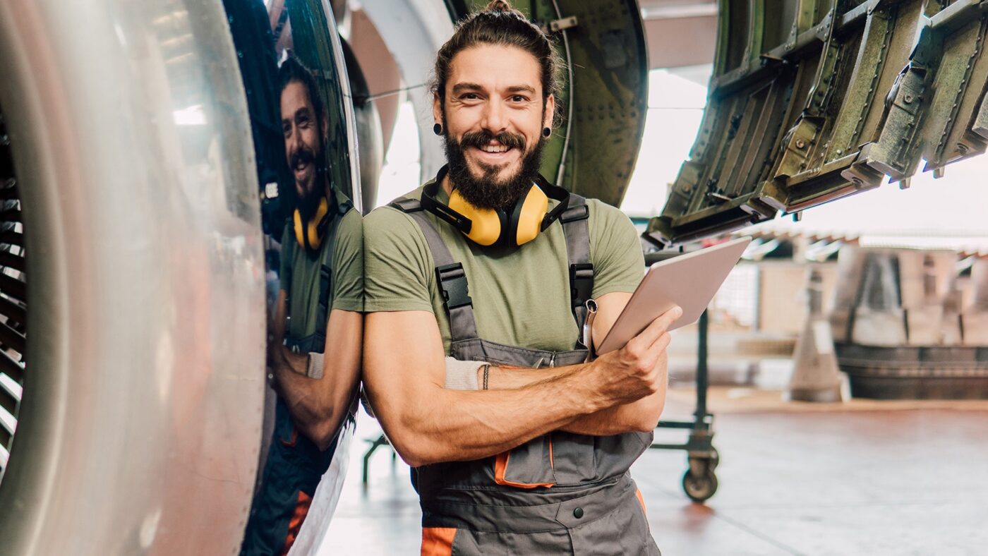 Mecánico industrial sonriente con tablet junto a motor de avión