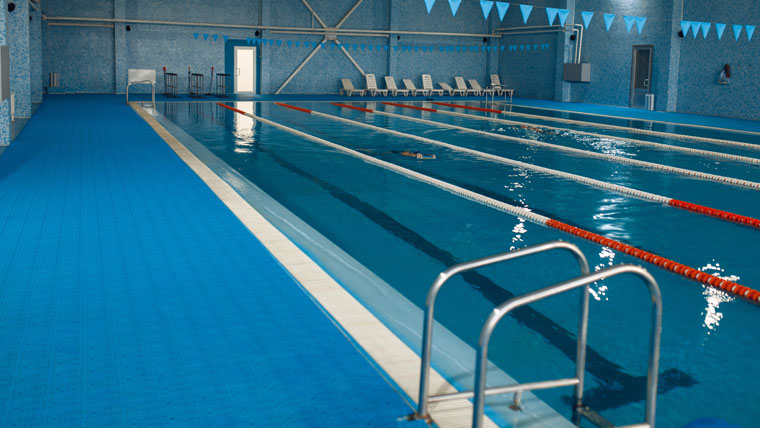 Piscina cubierta con carriles de natación, escalera metálica y tumbonas en el borde — cursos en Huelva