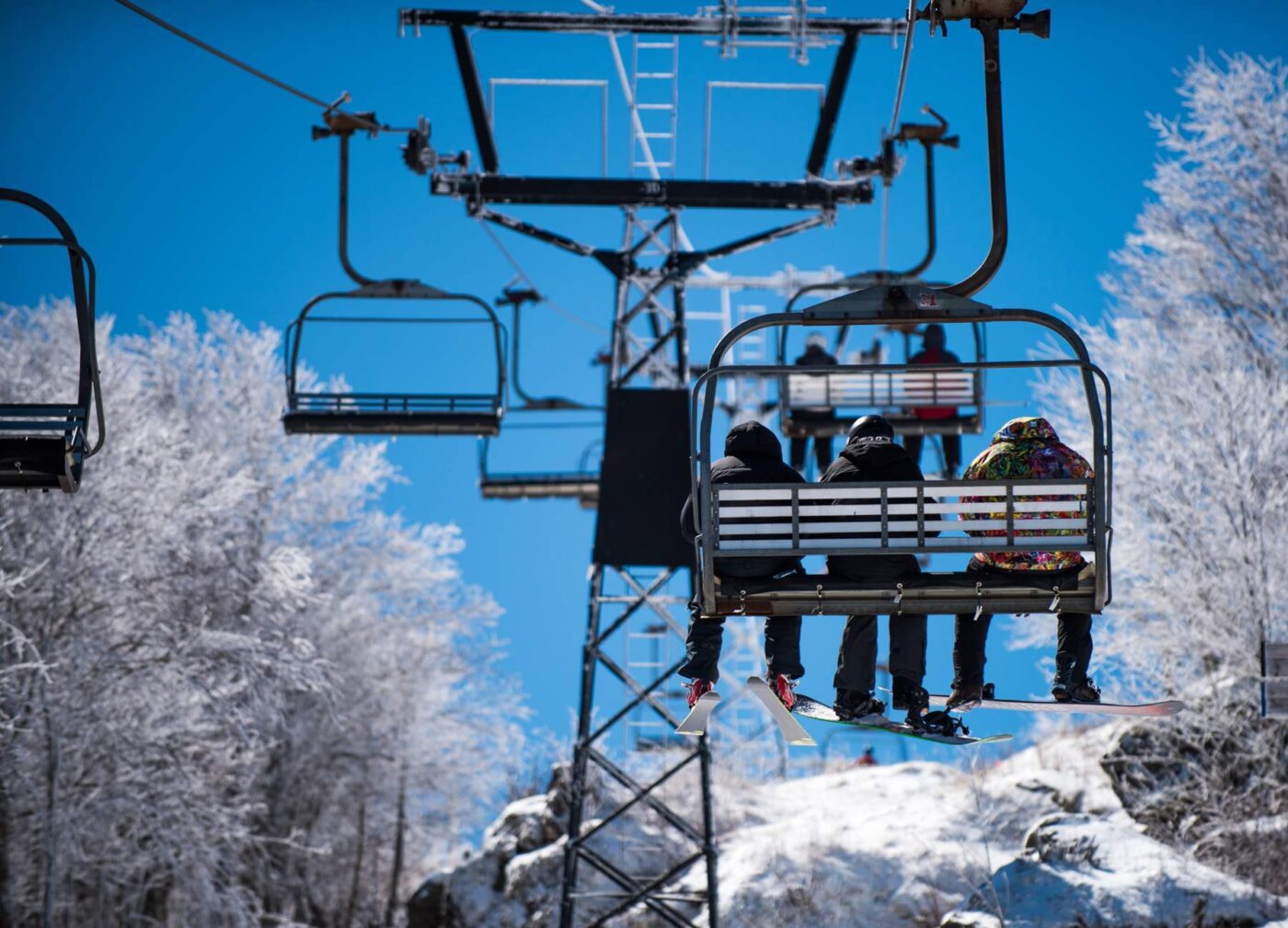 Telesilla con tres personas y tablas de snowboard entre árboles nevados — cursos online